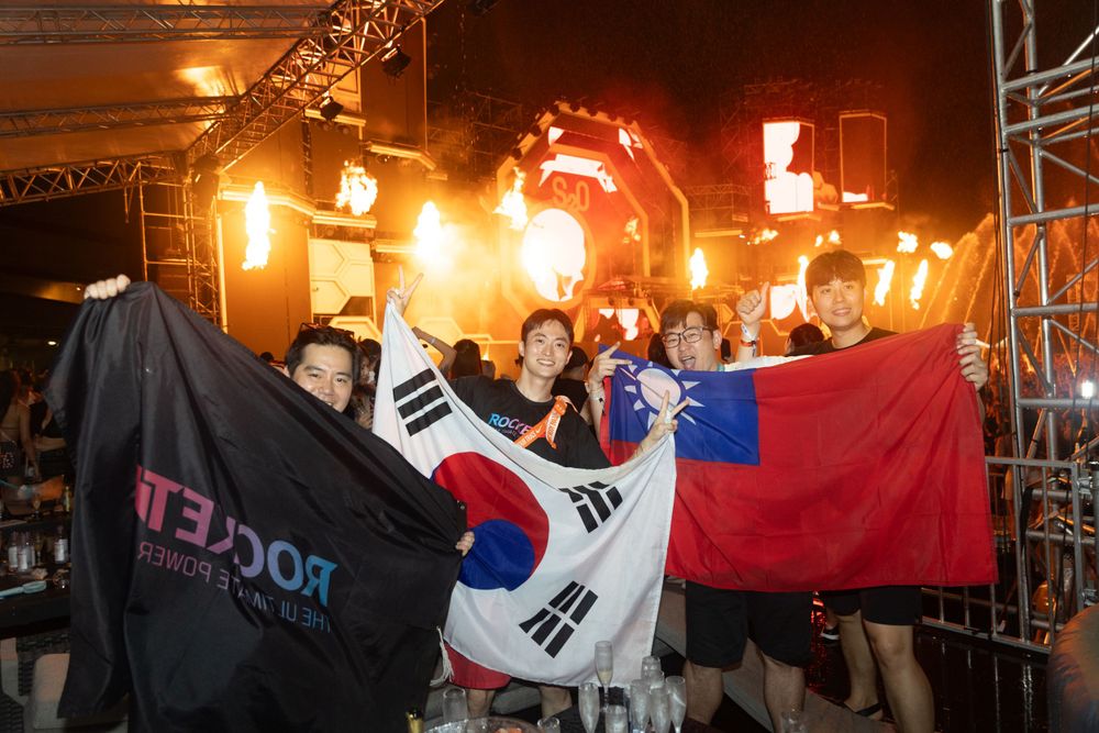 Group of friends holding Rocket banner with South Korean and Taiwanese flags at festival.