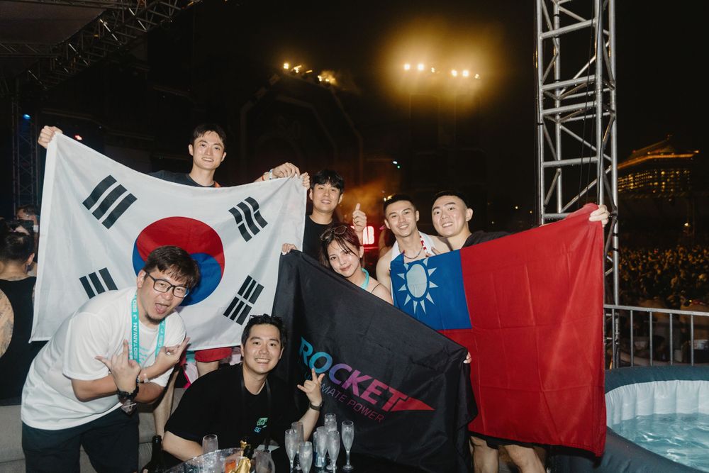 Excited group posing with South Korean and Taiwanese flags at nighttime outdoor concert.