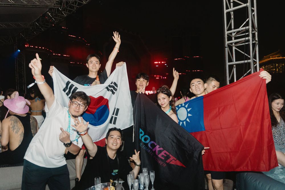 Group of friends celebrating with South Korean and Taiwanese flags at outdoor music festival.