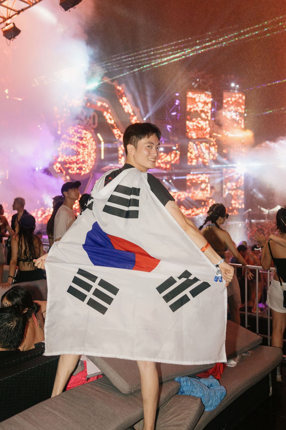 Man proudly displaying South Korean flag at colorful outdoor music festival at night.