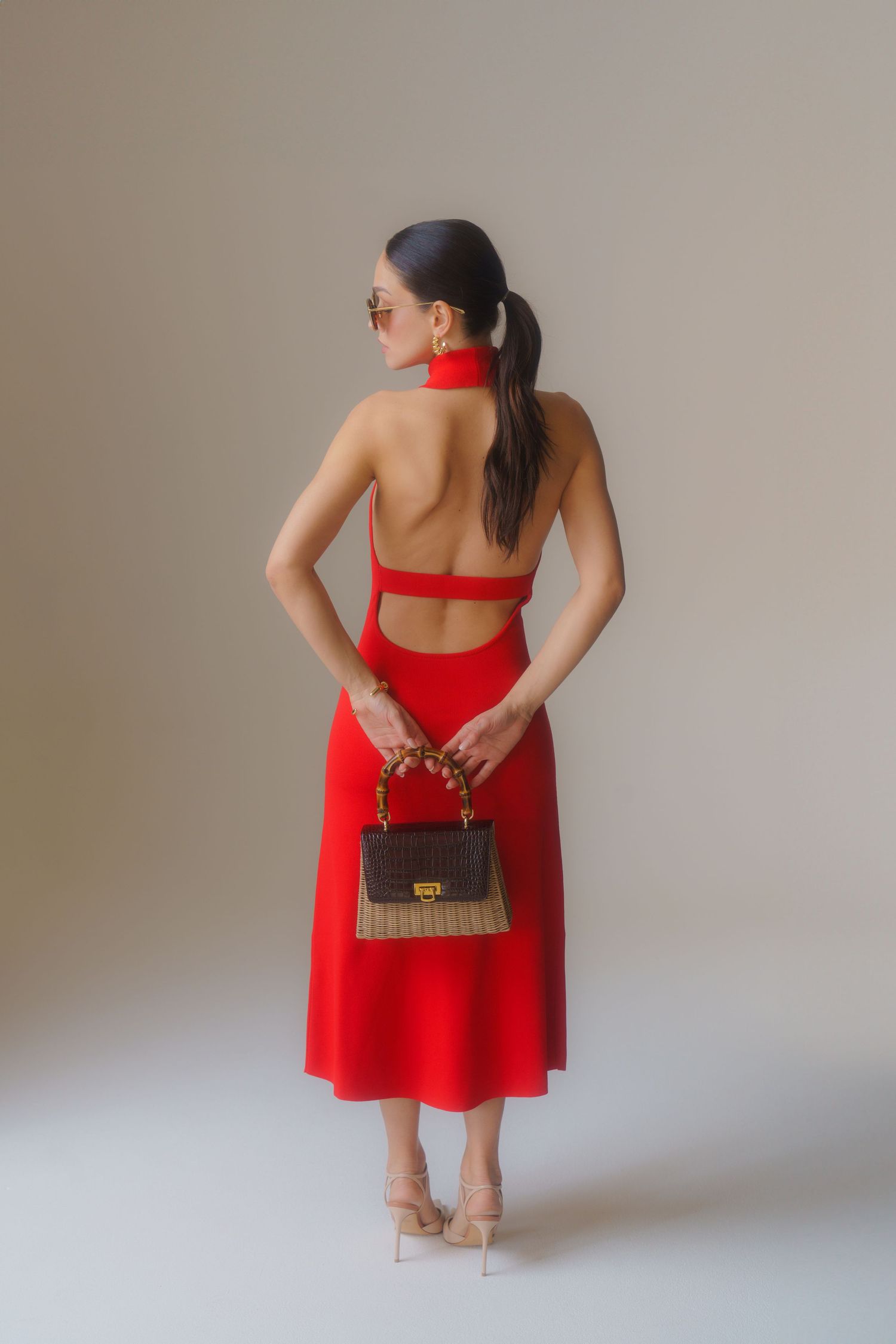 Fashion photo of red backless dress and designer handbag in studio setting.