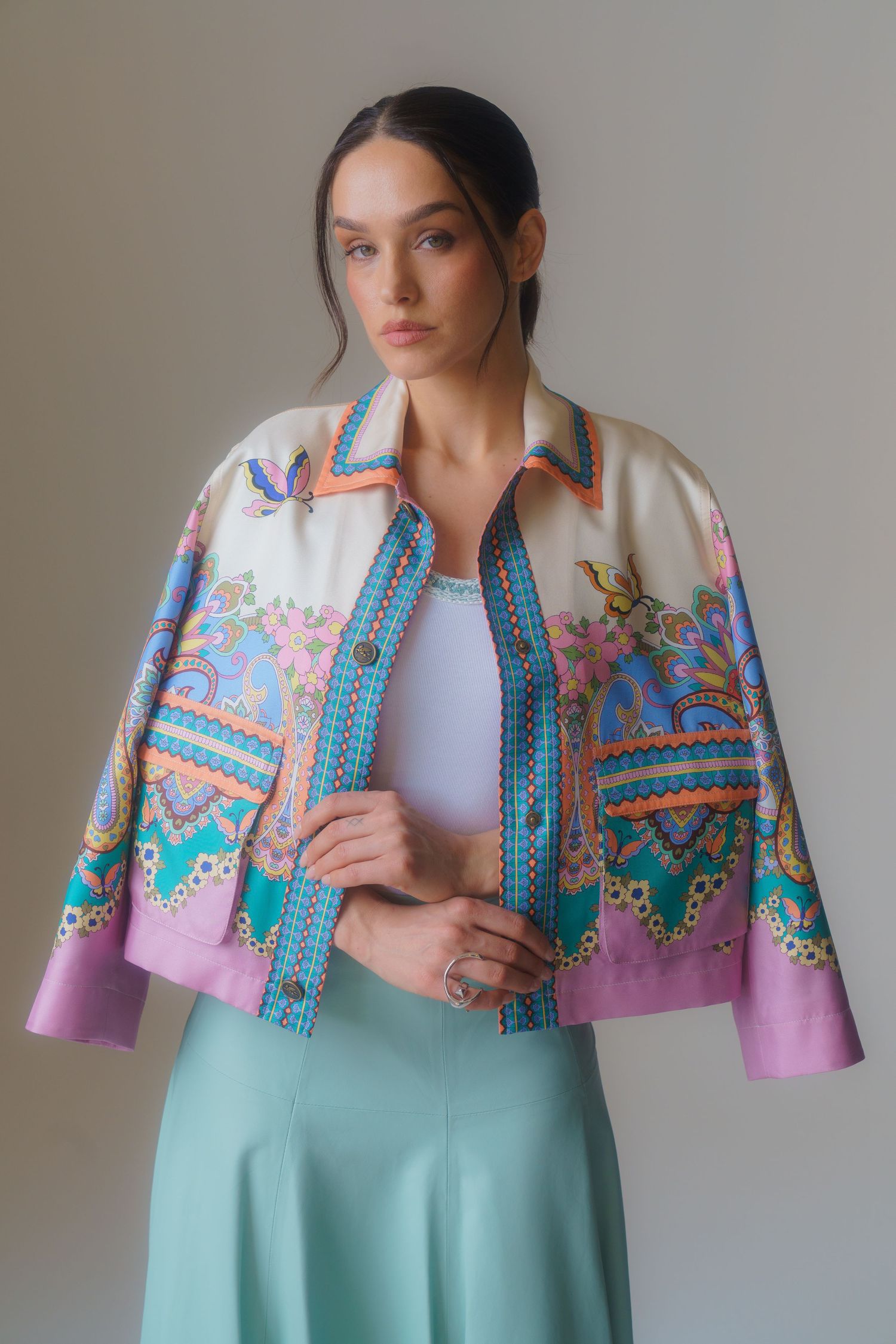 Fashion model wearing a vibrant printed cropped jacket with turquoise and pink patterns over white top and mint skirt.