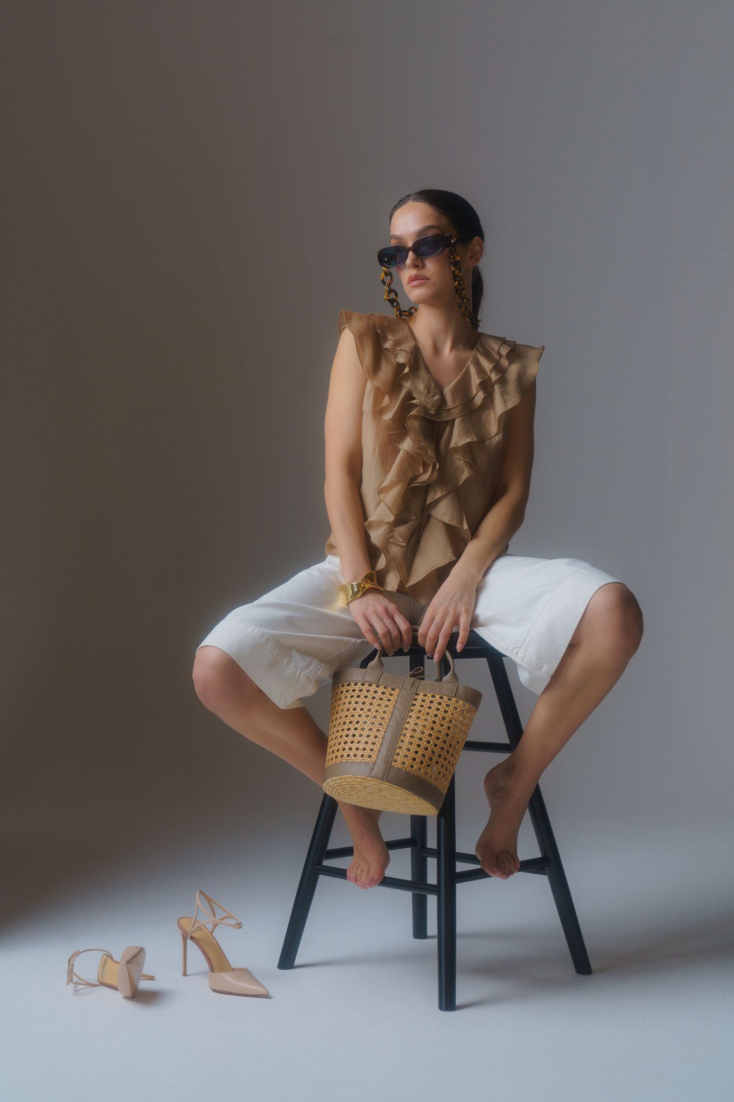 Studio fashion shot featuring beige ruffled top, white shorts, and woven handbag with sandals.