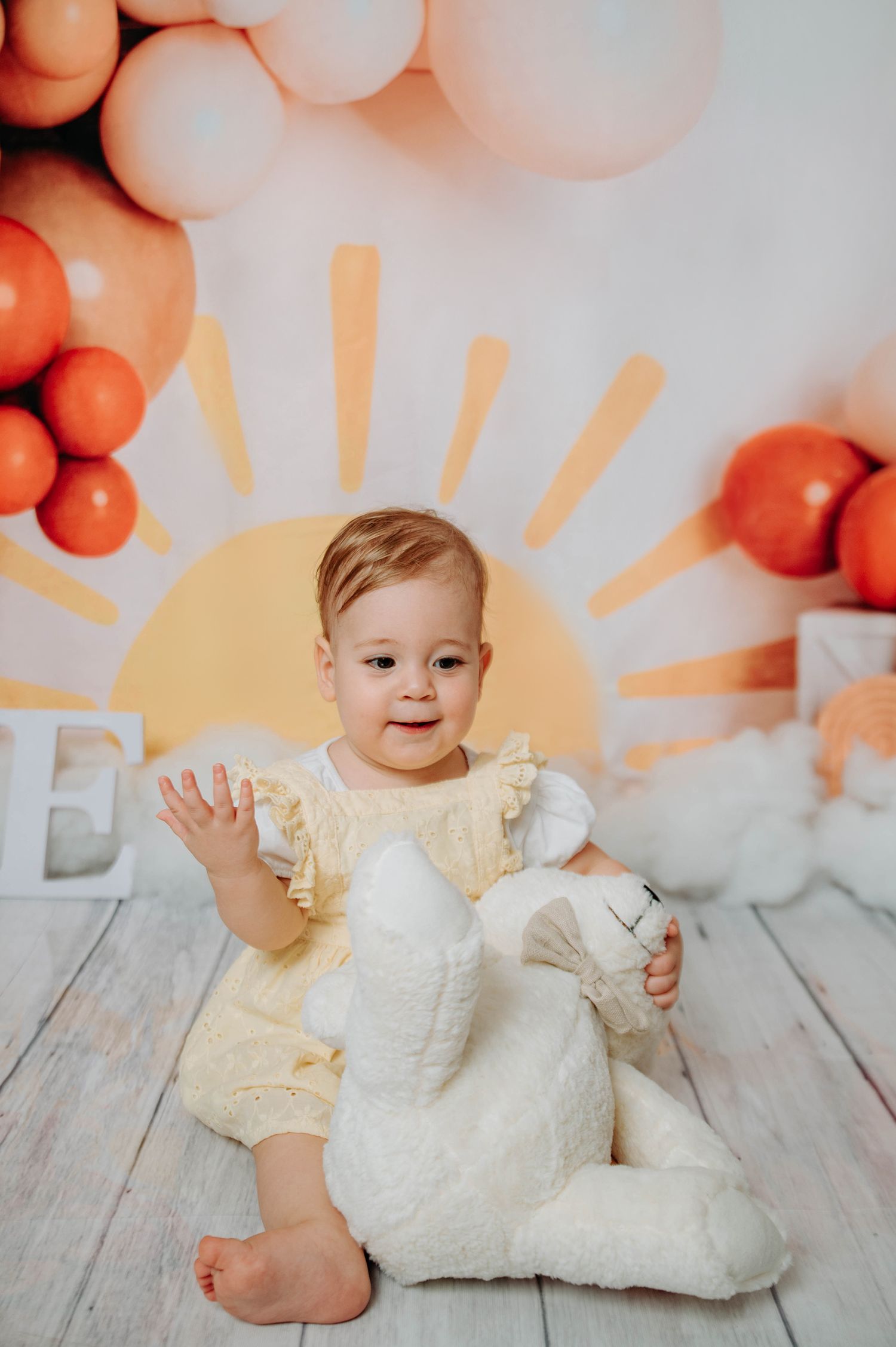 Yellow and orange balloon backdrop with sun rays design and white stuffed bunny.