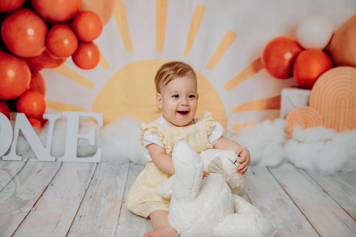 Bright orange balloon and sunshine backdrop with white wooden floor and ONE lettering.