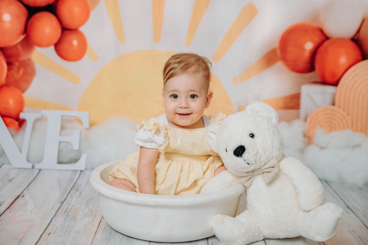 Professional photo setup with orange balloon arch, sunburst background and white teddy bear.