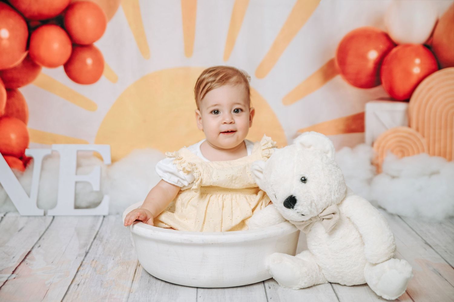 Studio portrait setup with orange balloons, sun rays backdrop and white plush bear.
