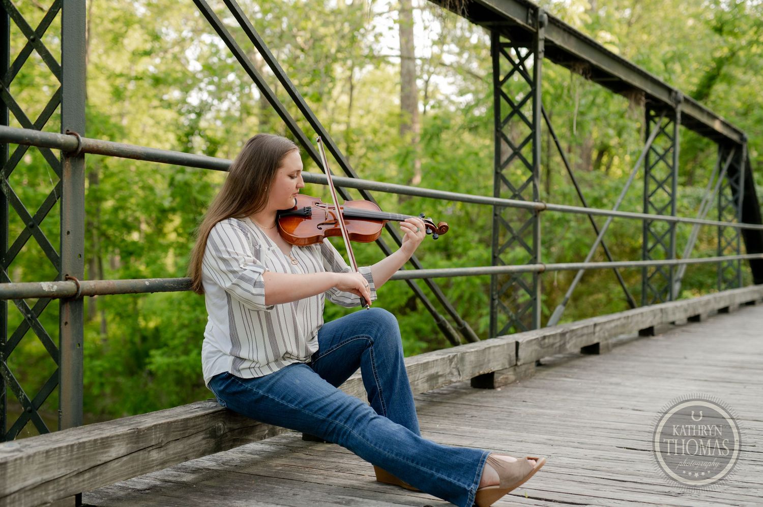 Musician performs on violin while seated on rustic bridge with metal framework.