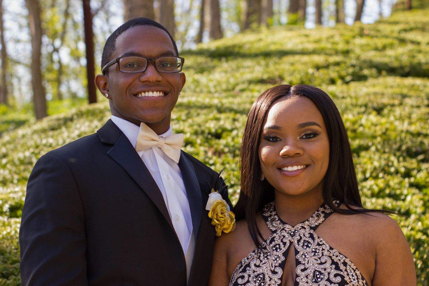 Young couple in formal wear smiles brightly against spring garden background.