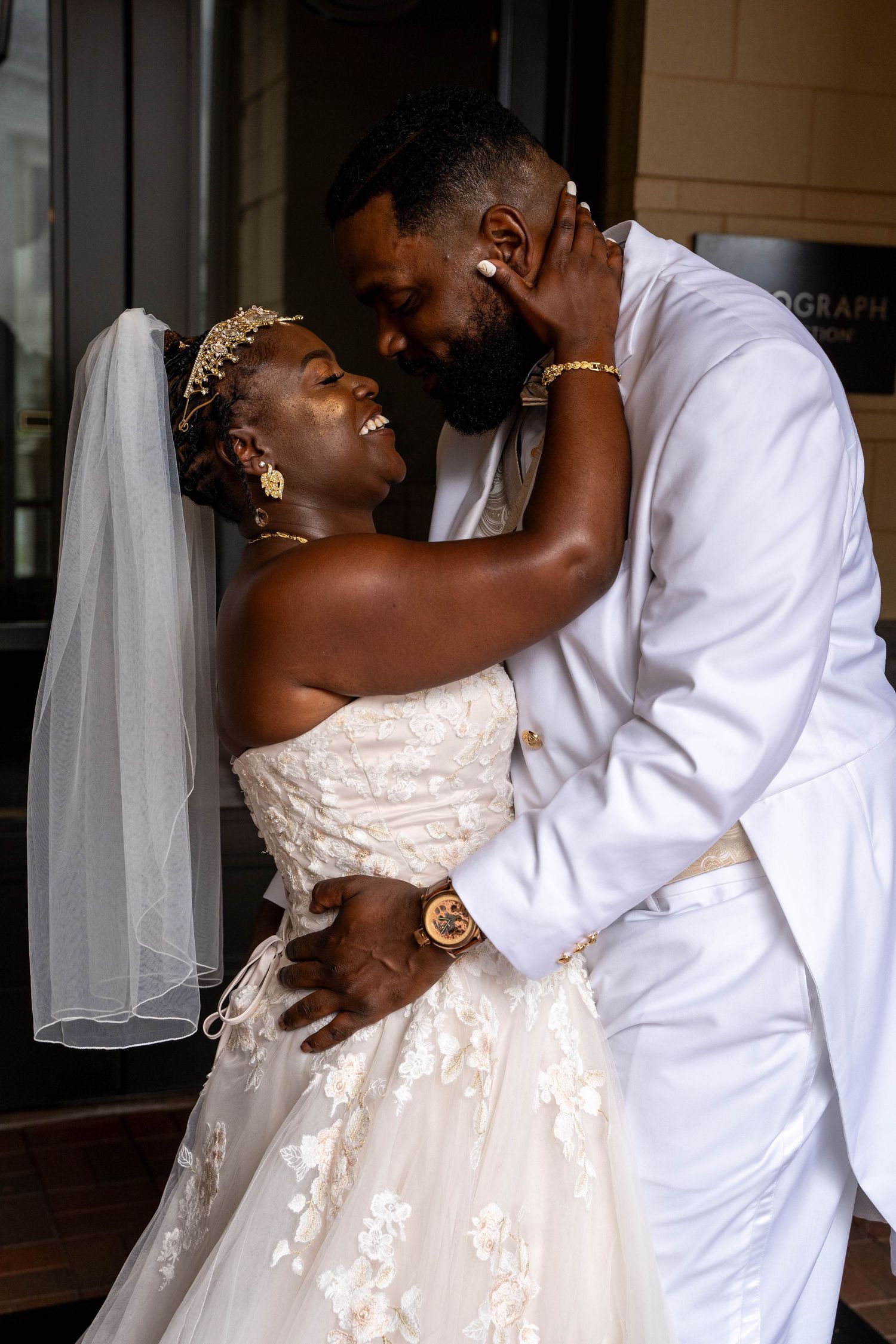 A loving couple shares an intimate moment on their wedding day, with the bride in a white lace gown and veil.