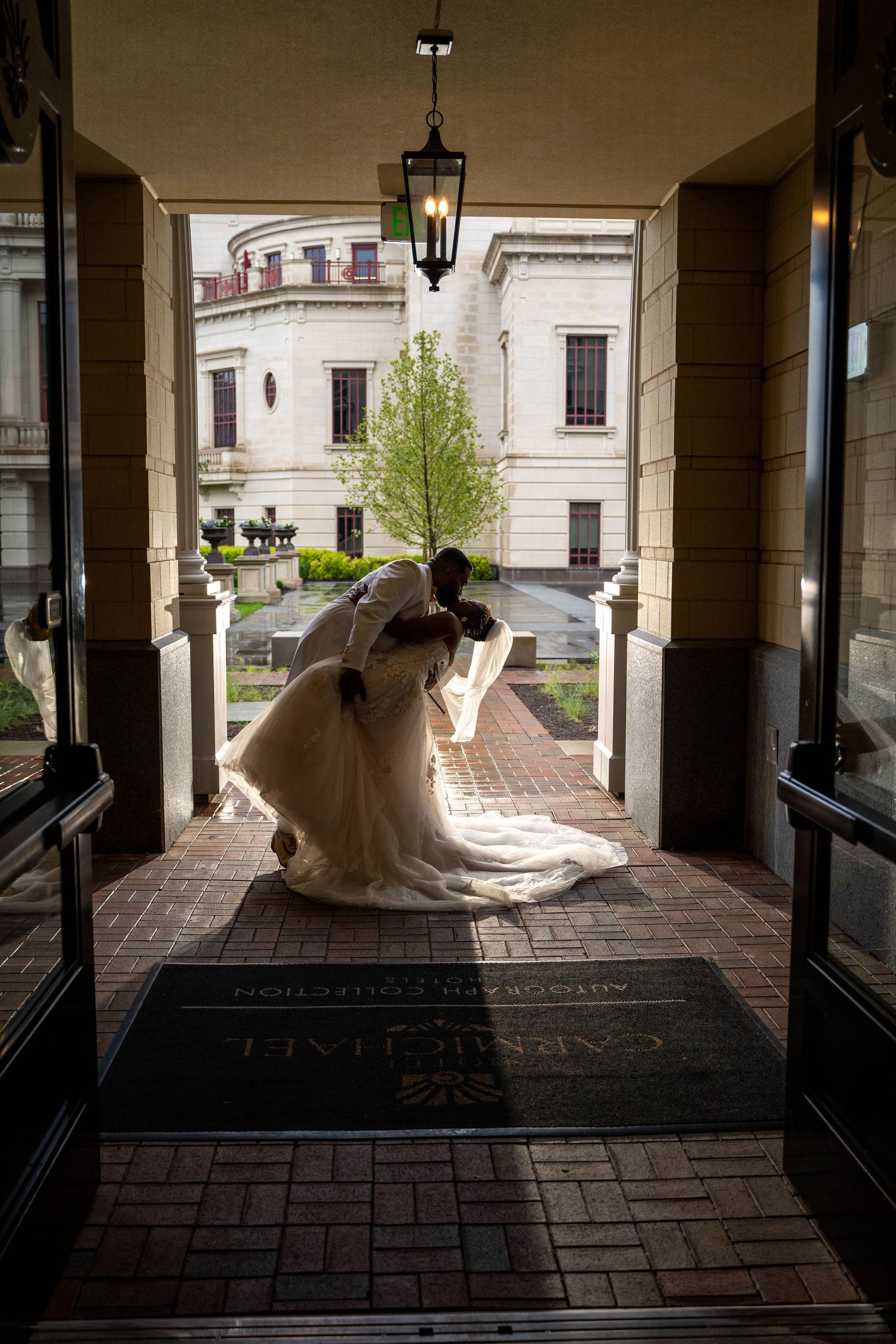 A romantic wedding silhouette captured in an elegant portico entrance with a hanging lantern and brick courtyard.