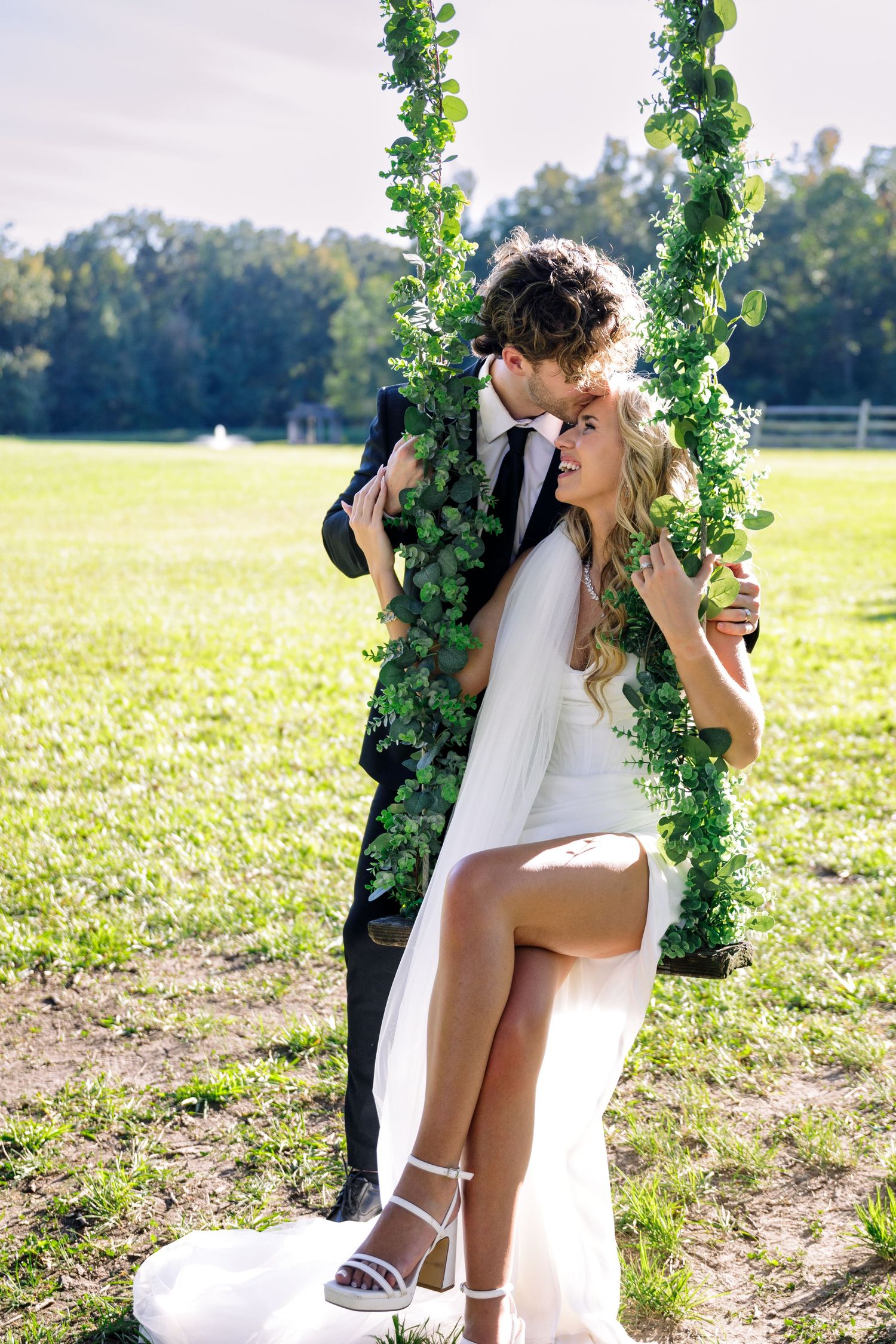 Wedding couple shares romantic moments by an ivy-covered garden arch in a sunny field.