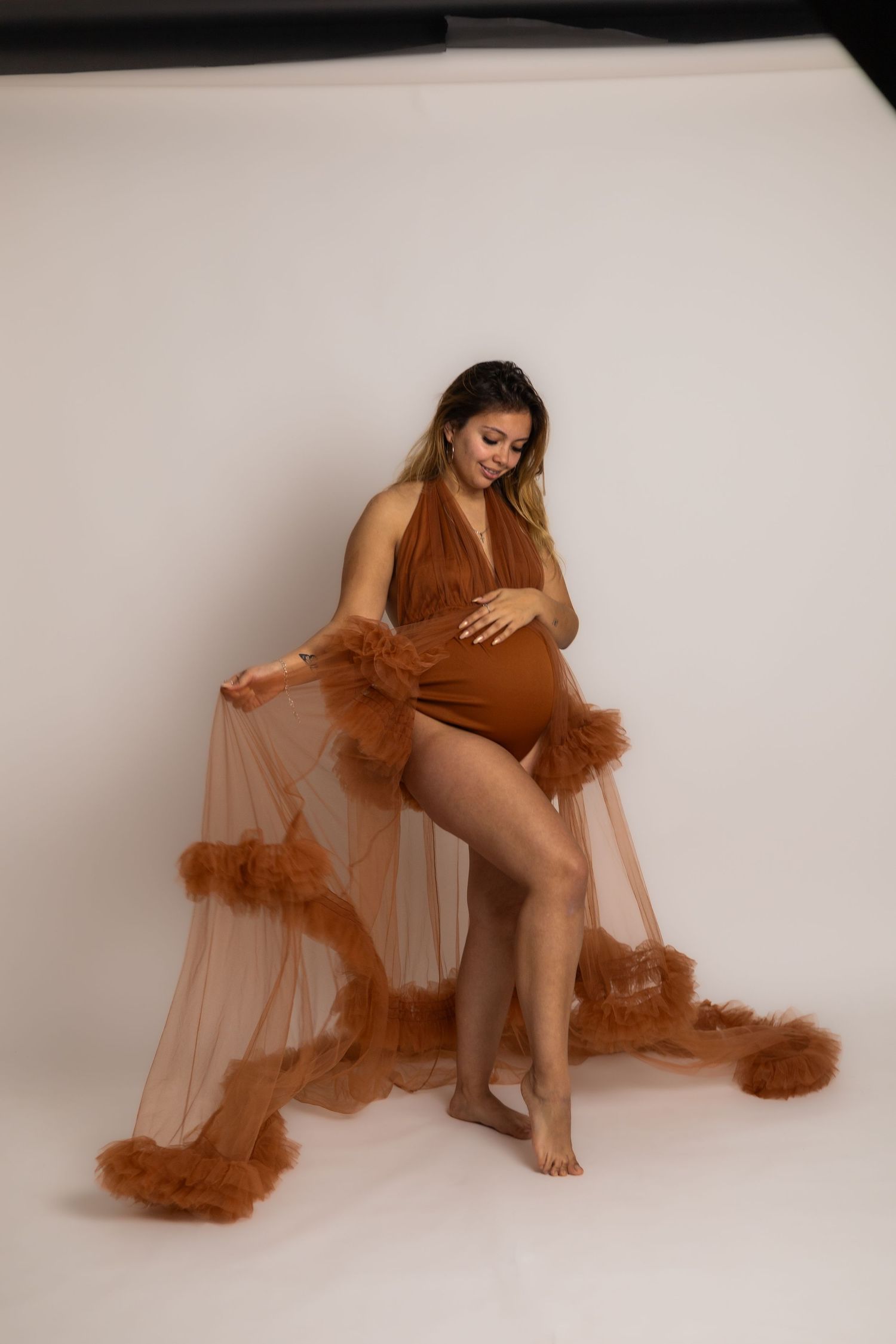 Artistic maternity portraits with flowing brown tulle fabric against white backdrop.