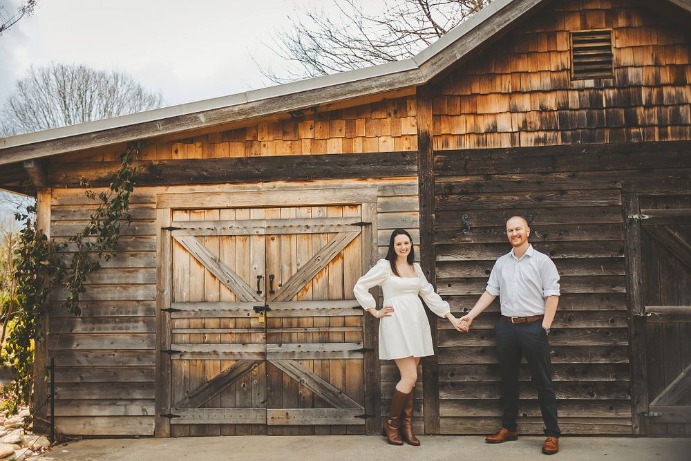 Couple holding hands in front of rustic barn with cedar shake siding.
