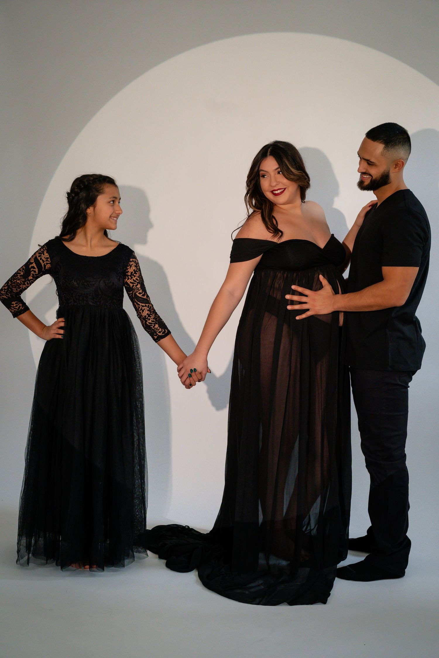 Maternity photoshoot with couple in black attire showing silhouettes against white background.