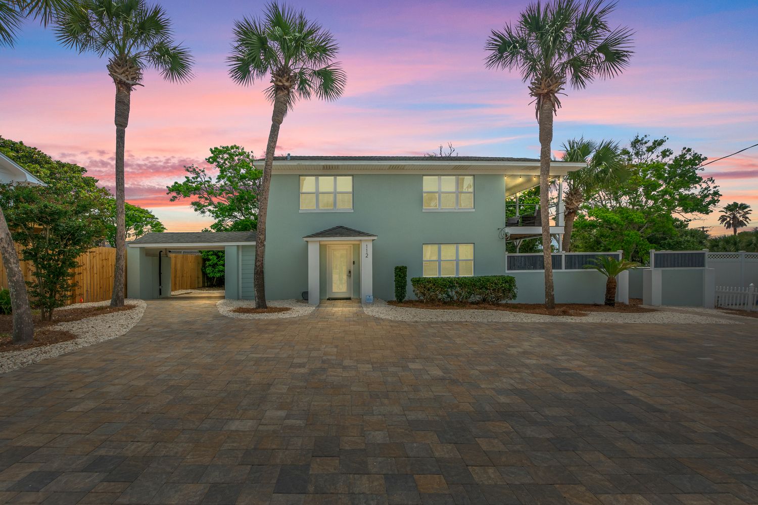Modern two-story waterfront home with palm trees and paver driveway at sunset in Florida.