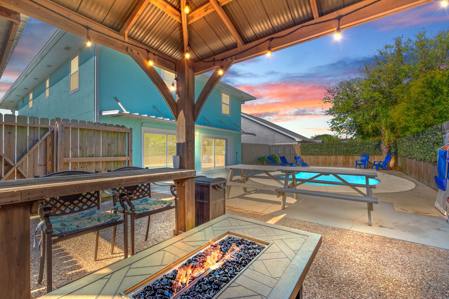 Covered outdoor patio with modern fire pit and pool view at sunset creates a cozy entertaining space.