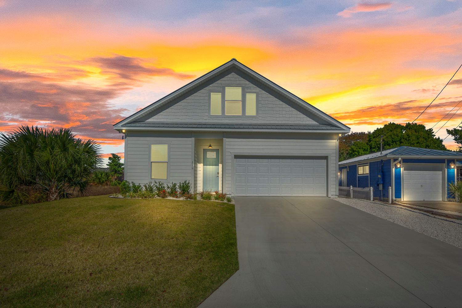 Gray house exterior with garage illuminated by dramatic sunset sky.