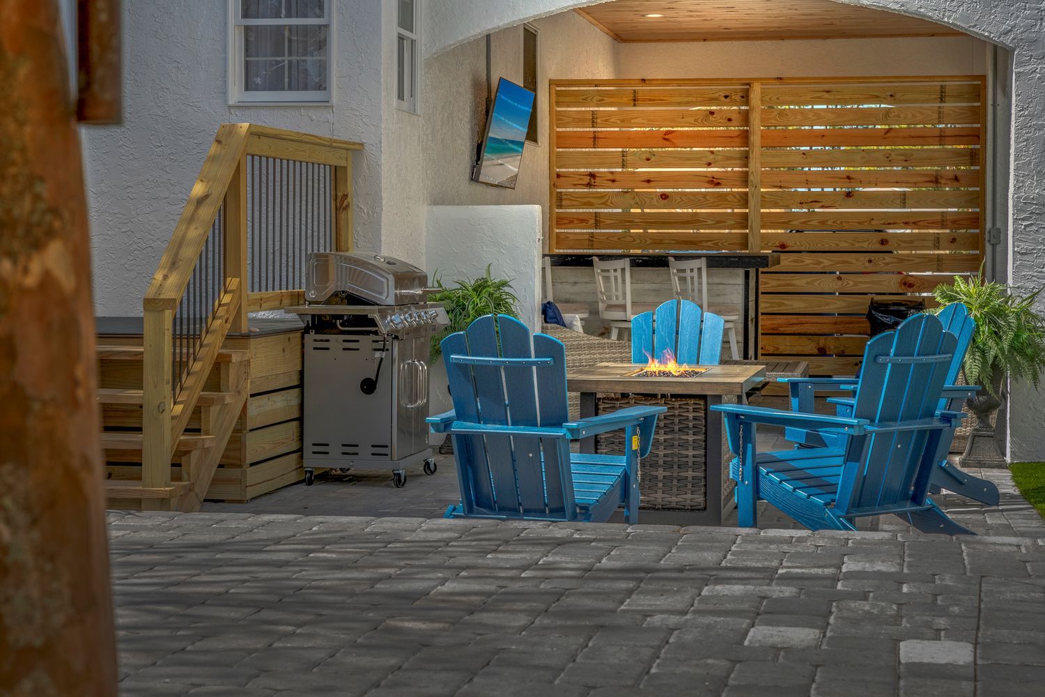 Cozy outdoor patio setup with bright blue Adirondack chairs and wooden privacy wall on stone pavers.