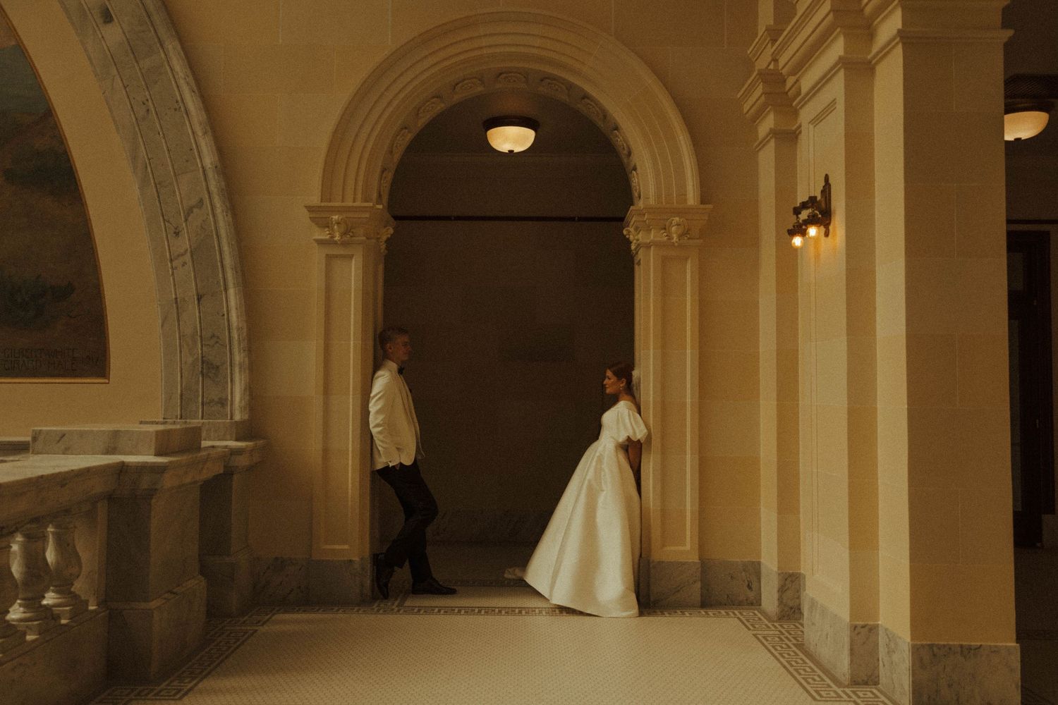 A wedding dress flows through arched hallways of a historic building with warm lighting.