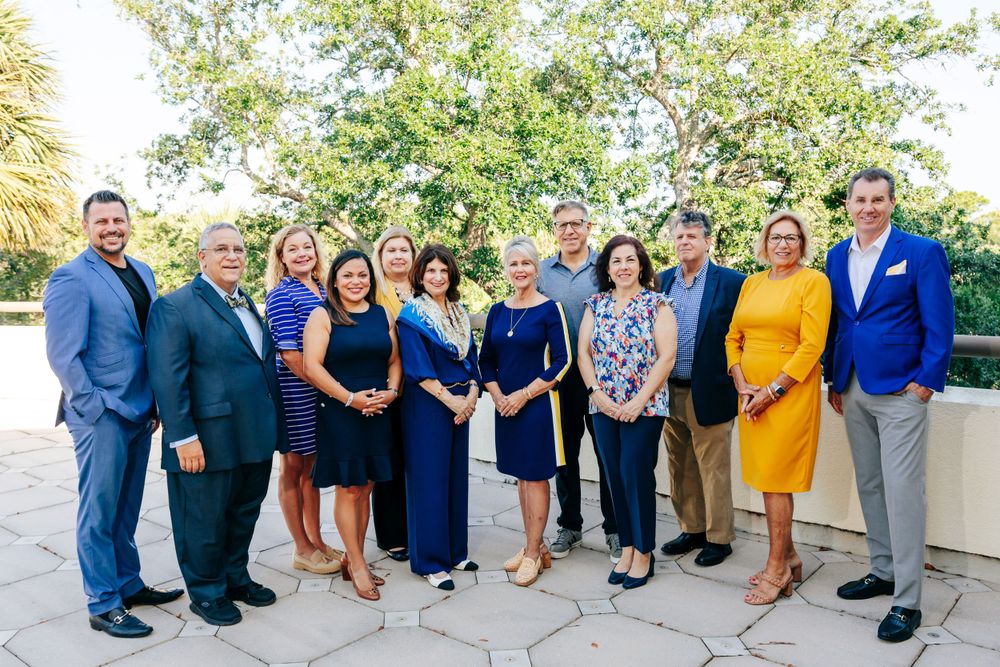 Professional group photo of team members dressed in business attire standing together outdoors.