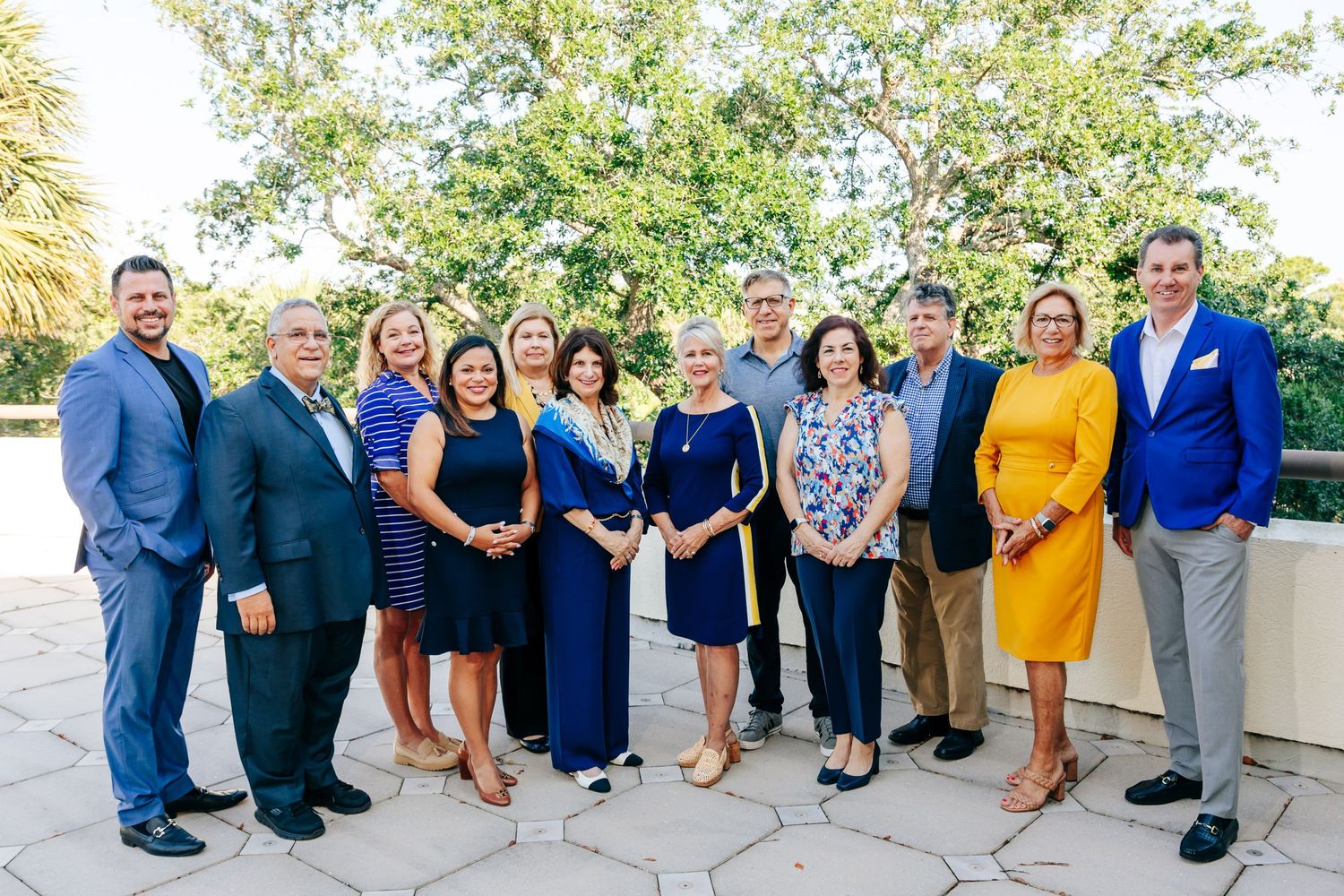 Professional group photo of team members dressed in business attire standing together outdoors.