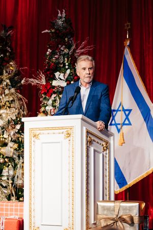 Speaker at podium with Israeli flag and decorated Christmas tree in formal setting.