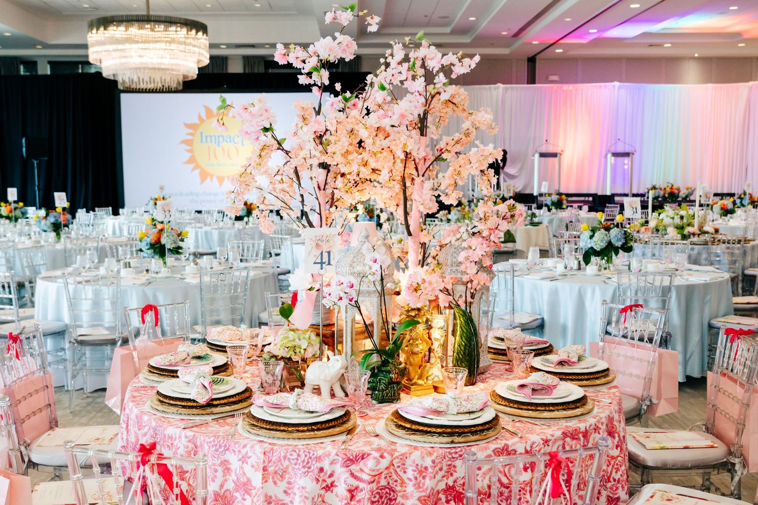 Elegant wedding reception table with pink floral centerpiece and crystal chandelier overhead.