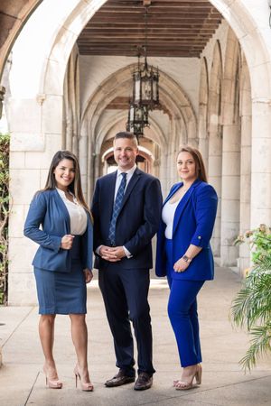 Three professionals in business attire pose under arched stone corridor.