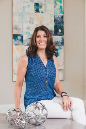 Woman in polka dot blouse sitting beside decorative silver spheres against abstract art.