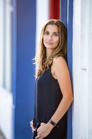 Professional portrait against blue and white striped wall wearing sleeveless dark top.