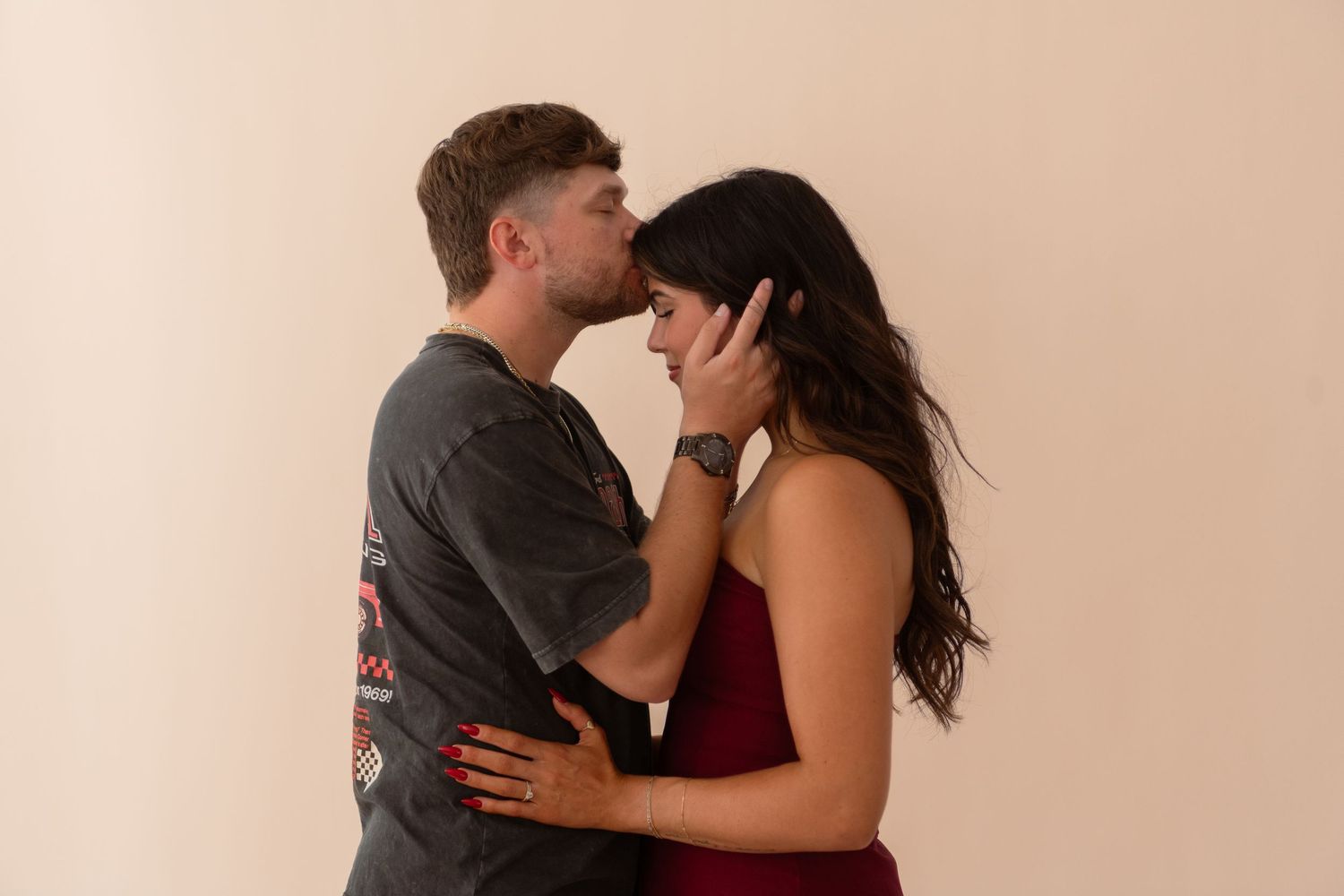 Couple sharing a tender kiss, woman in burgundy dress embraced by man in graphic gray tee.