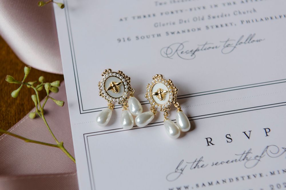 Pearl drop and crystal stud wedding earrings rest on an elegant white RSVP card with delicate floral decor.