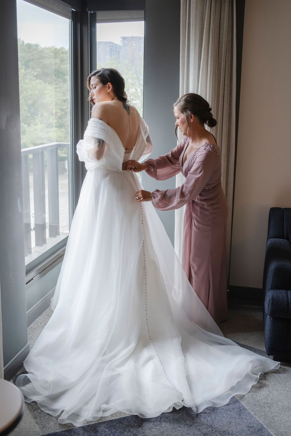 A wedding dress fitting in a bright room as someone wearing pink helps adjust the flowing white gown.
