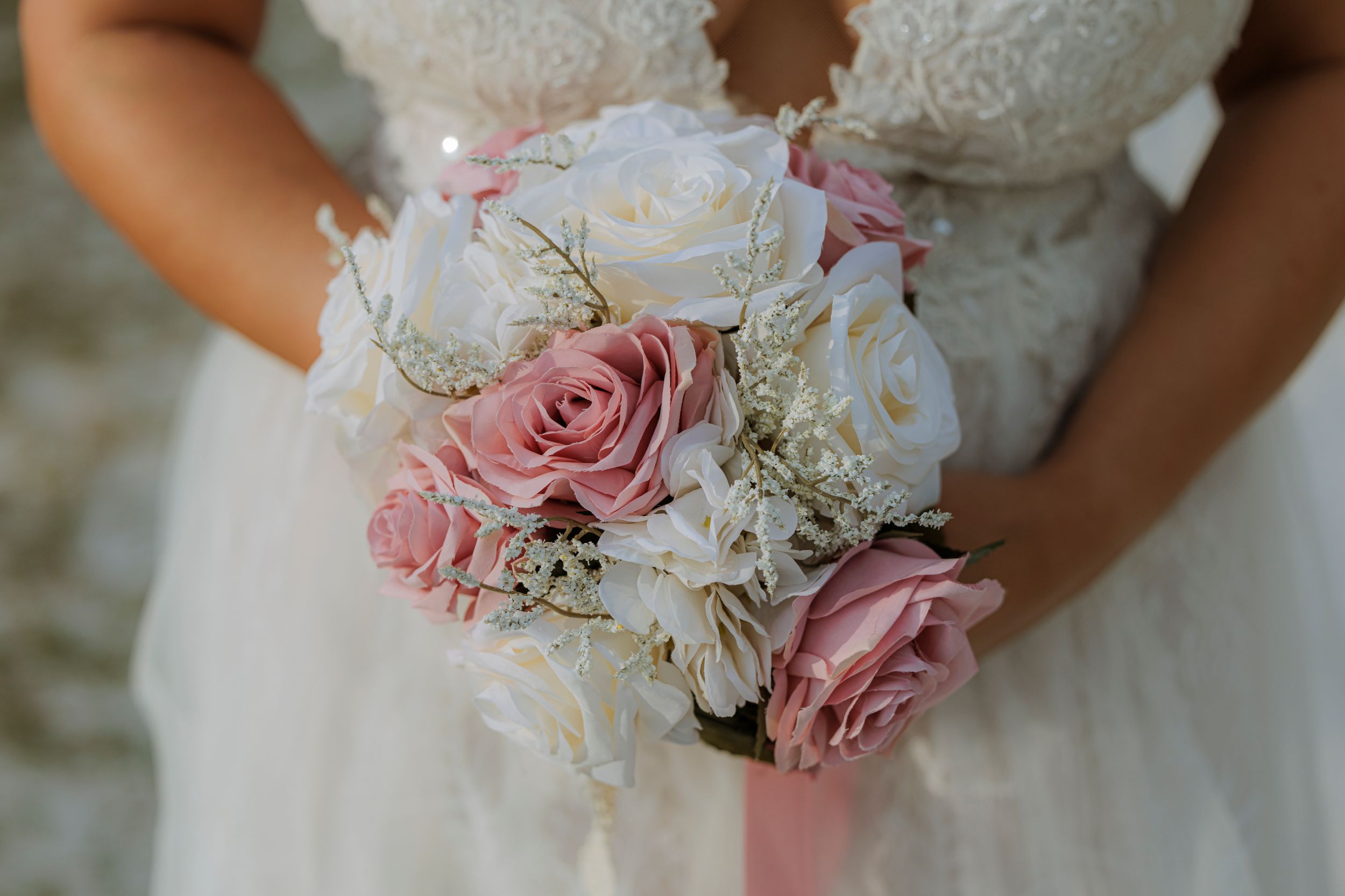 Bride holding romantic bouquet of pink and white roses with baby's breath and lace wedding dress detail.