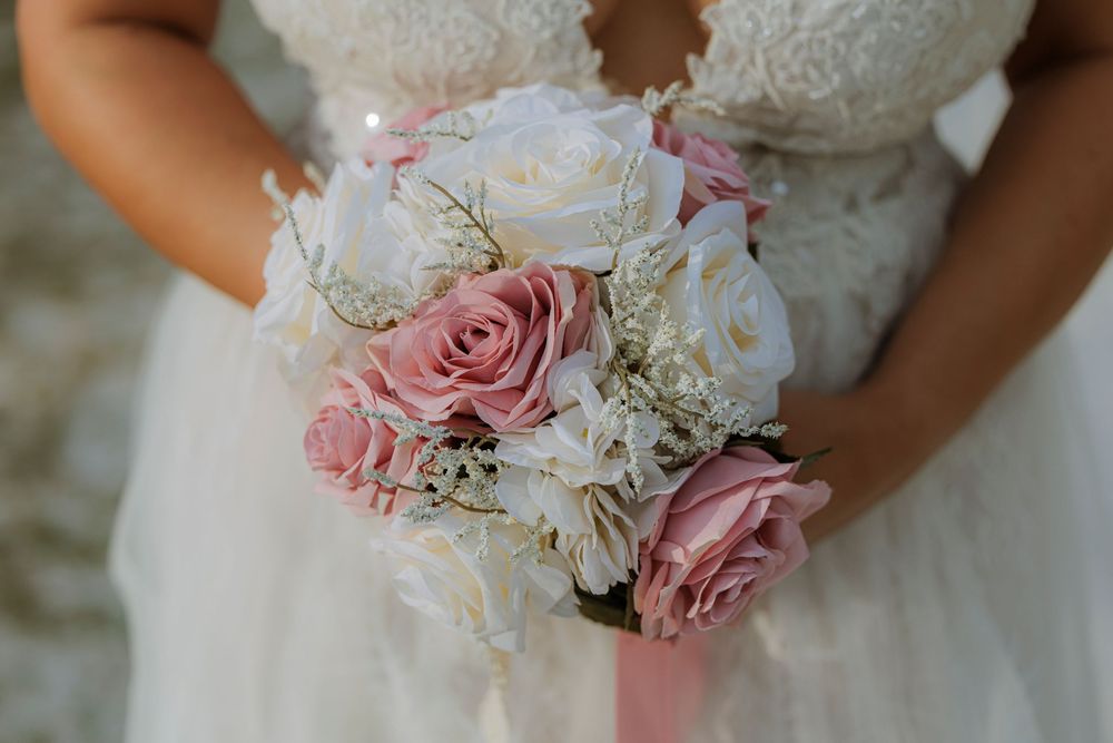 Bride holding romantic bouquet of pink and white roses with baby's breath and lace wedding dress detail.