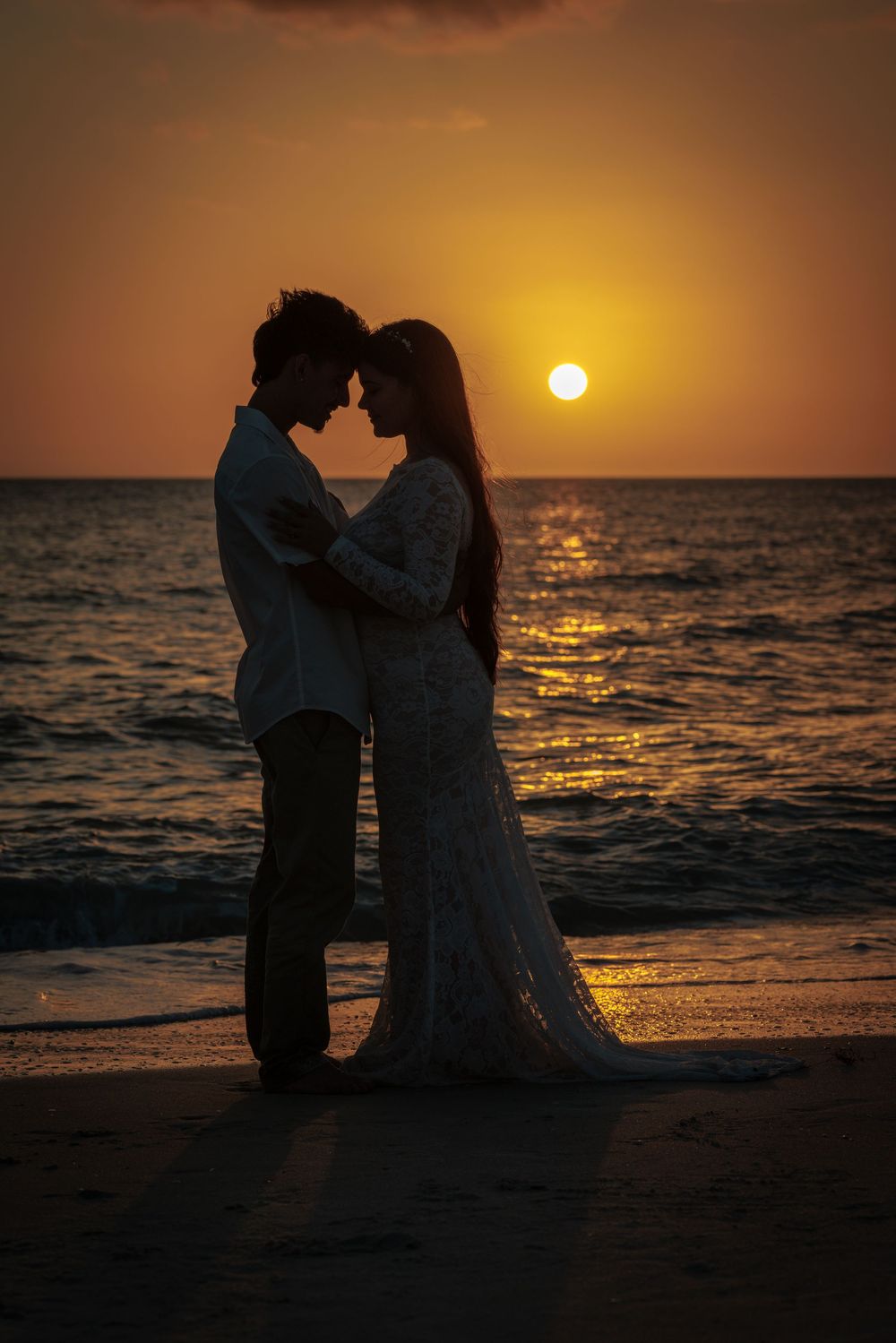 Romantic silhouette of bride and groom embracing at sunset on beach with golden sky.