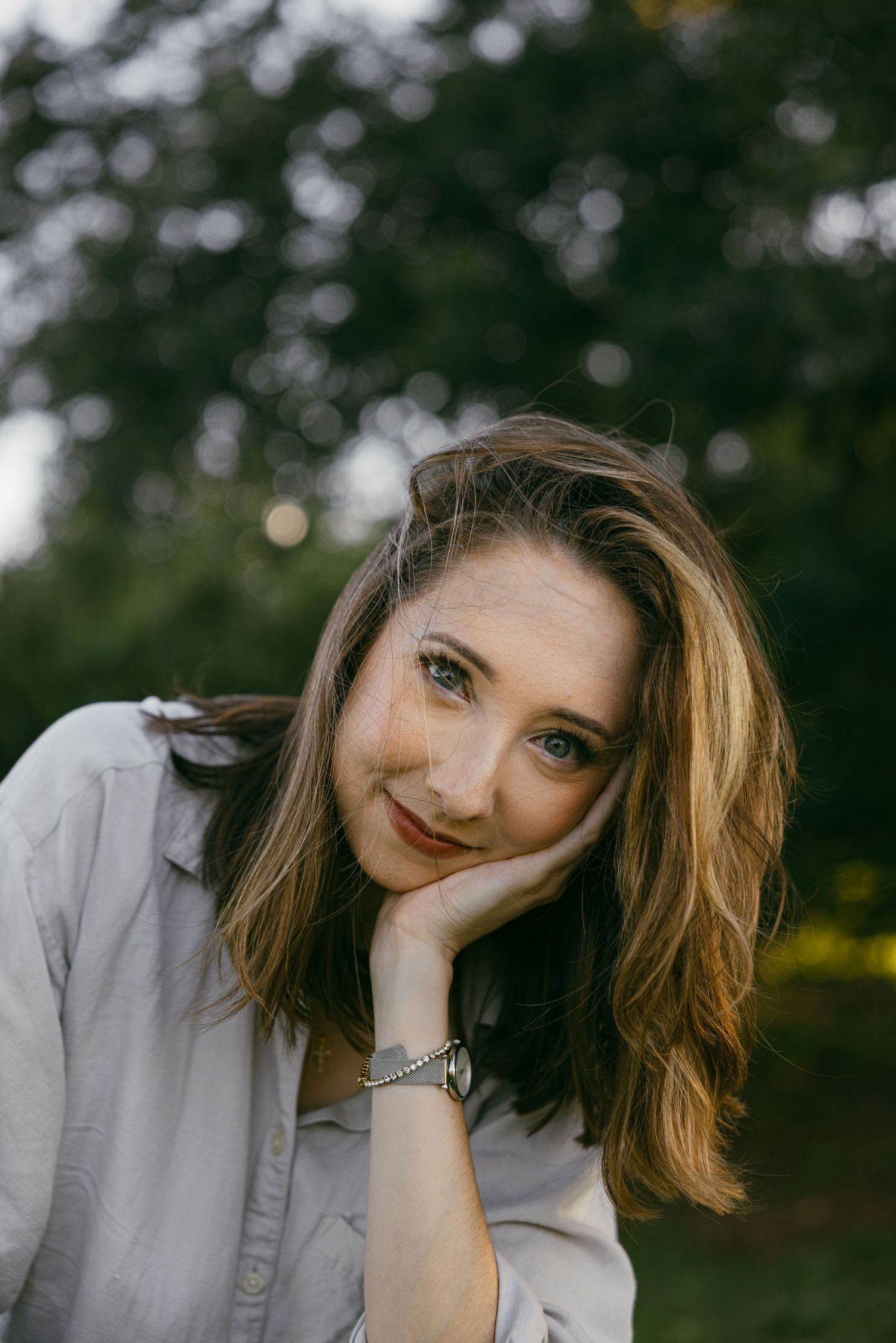 Woman with long wavy hair lying on grass with hand on face and peaceful expression.