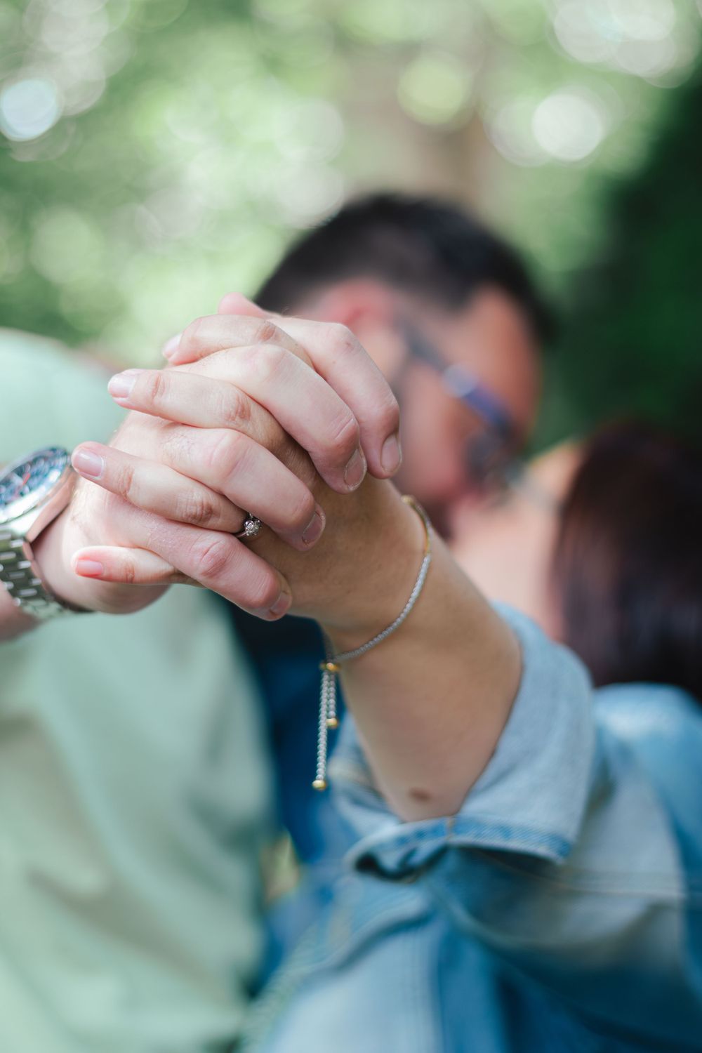 Close-up of clasped hands wearing jewelry against a blurred green background.