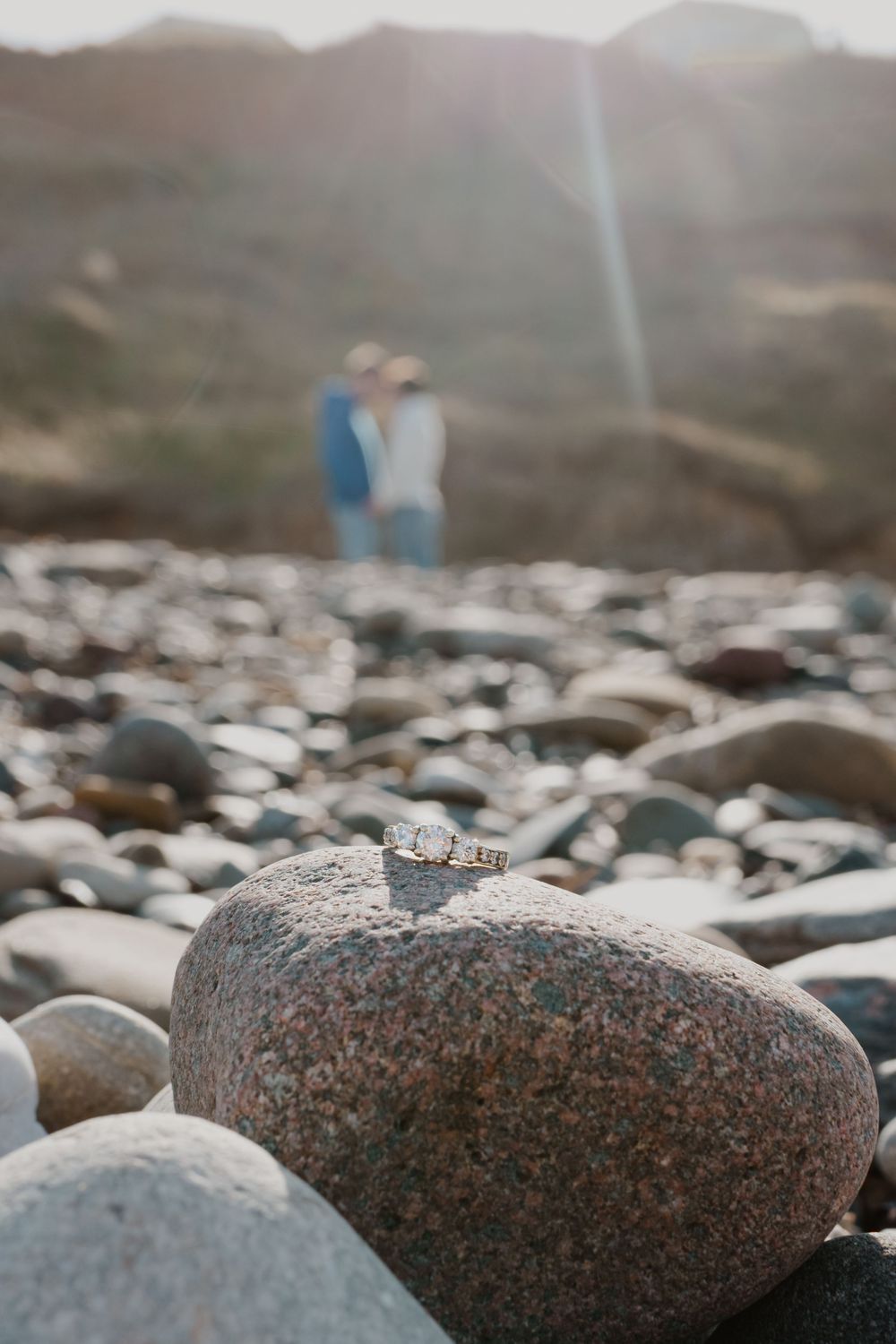 Close-up view of smooth granite rocks on a foggy beach with blurred mountains in the background.