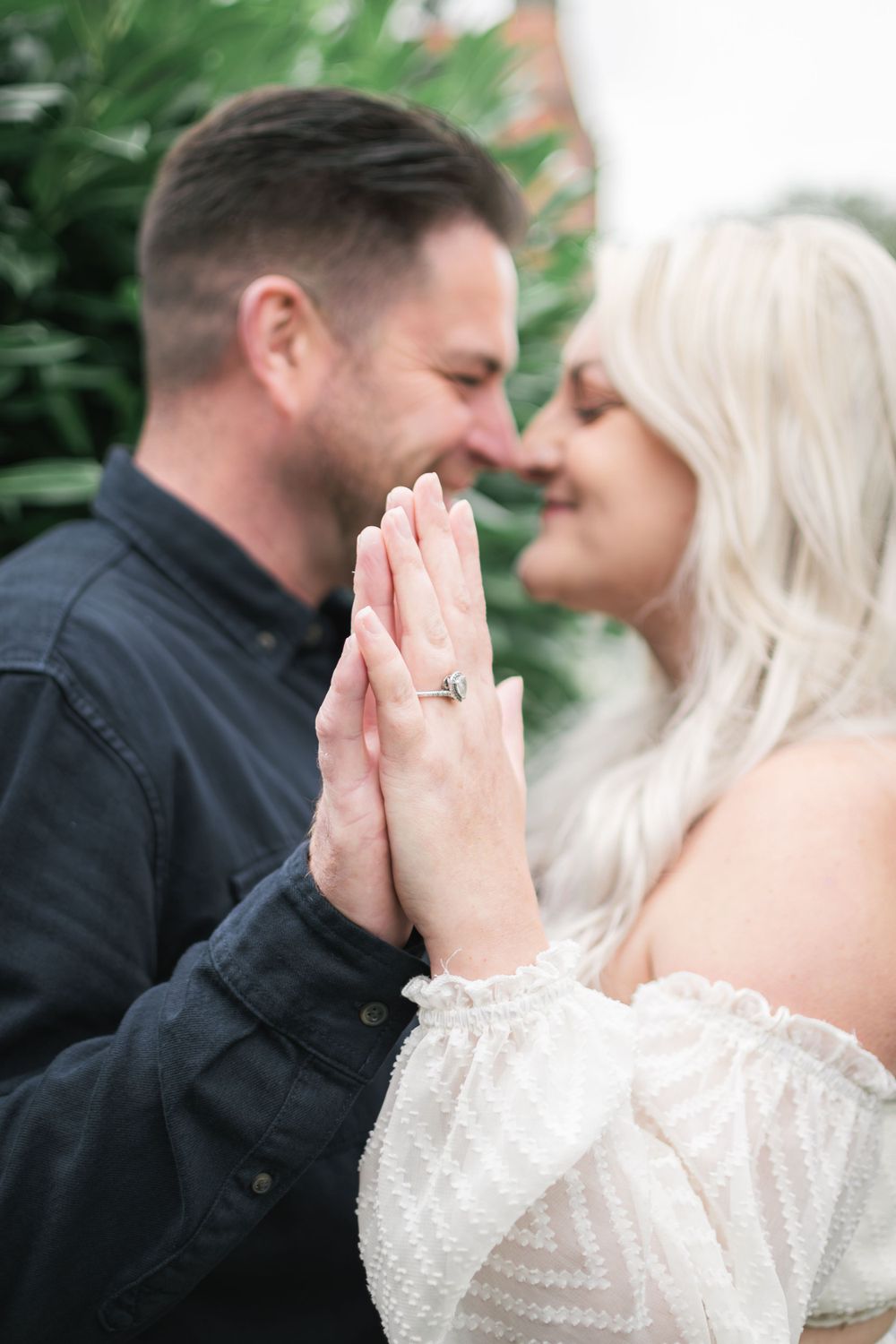 A romantic couple sharing an intimate moment while showing off an engagement ring in a garden setting.