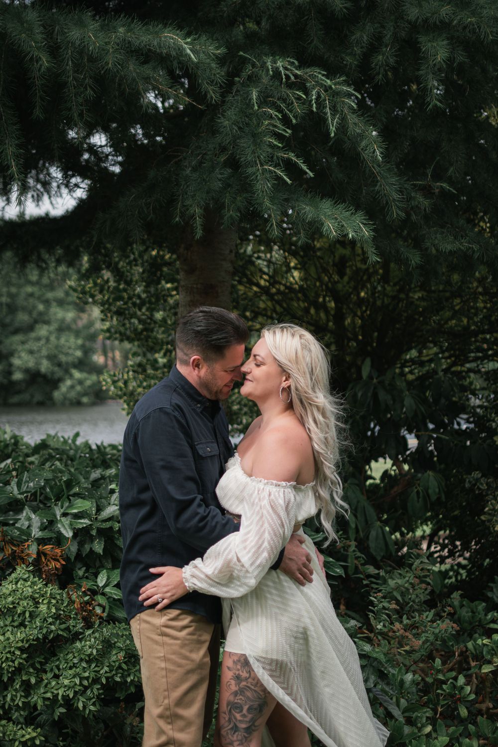 A couple embracing in a lush garden setting with evergreen trees in the background.