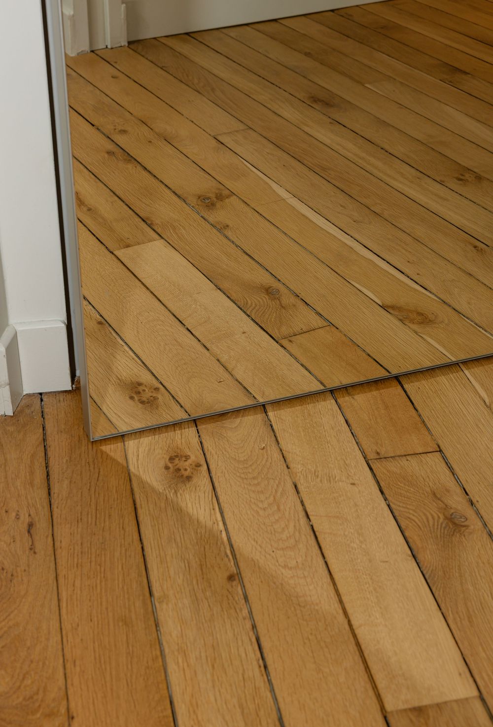 Warped and damaged hardwood flooring showing signs of water damage and buckling on light oak planks.