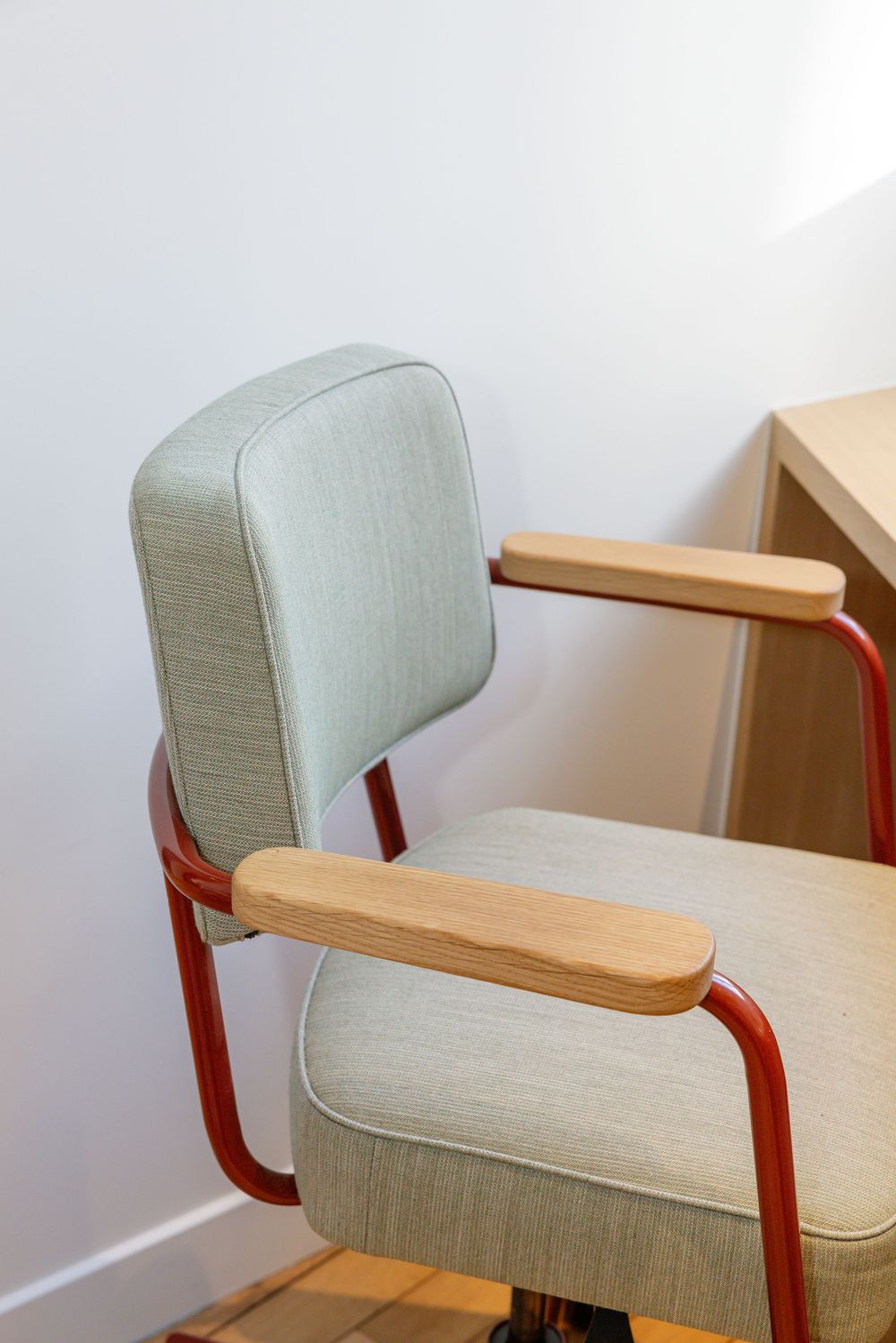 Vintage-style office chair with mint green upholstery, wooden armrests, and red metal frame against white wall.