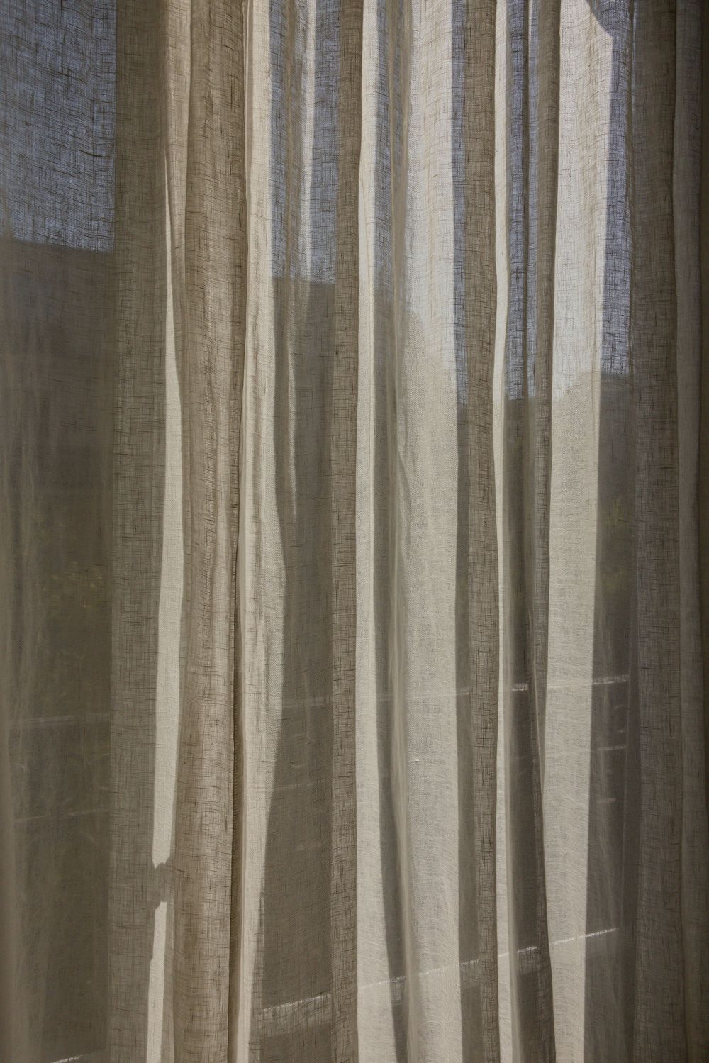 Light filtering through sheer white linen curtains creating soft vertical lines and shadows.