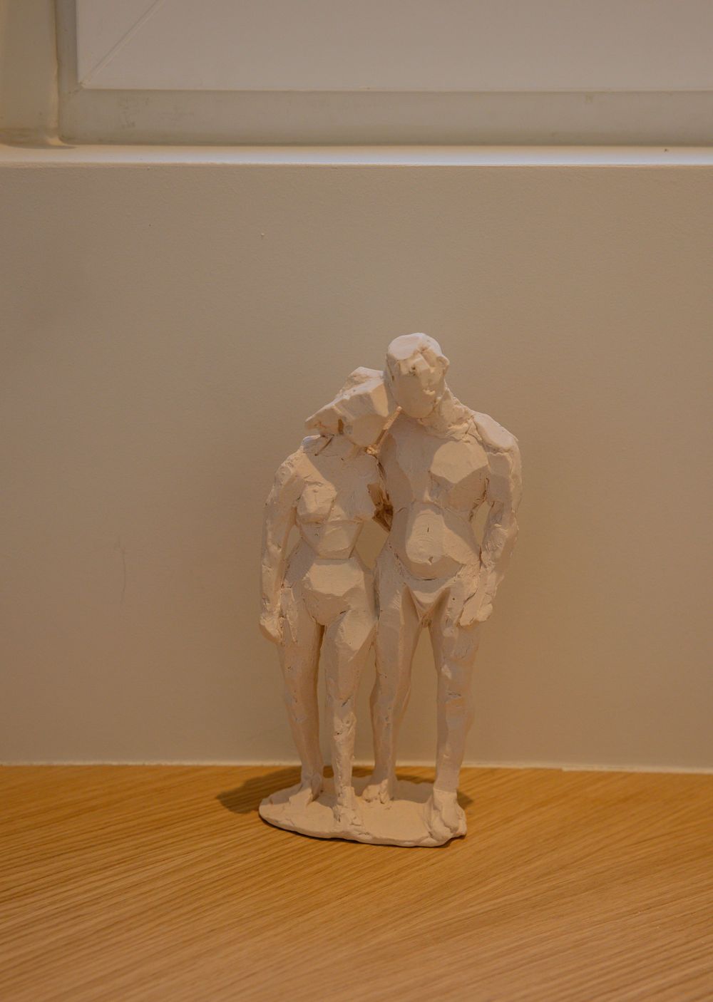 A series of clay or ceramic sculptures showing two figures embracing, displayed on a wooden floor against a beige wall.