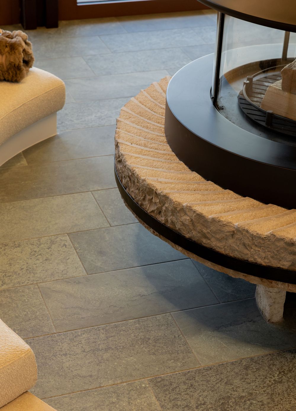 Close-up view of a curved stone bench with modern design elements against dark tile flooring in an interior space.