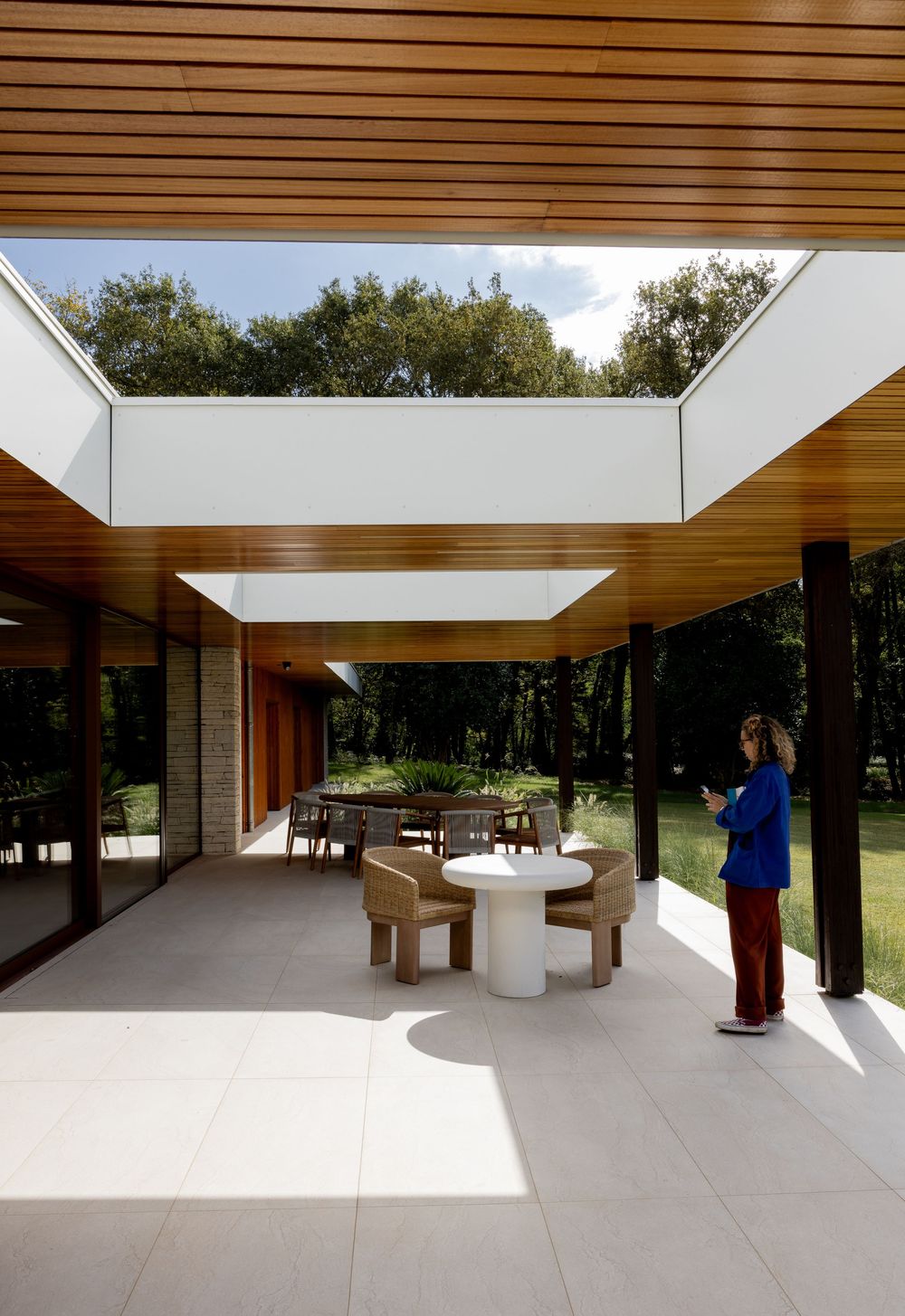 Modern minimalist interior space with glass walls, wooden ceiling beams, and natural lighting in a forest setting.