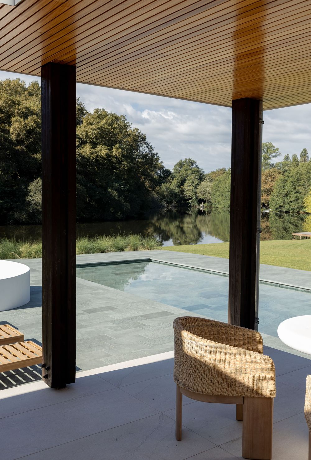 Modern covered patio area with wicker lounge chair overlooking an infinity pool and scenic natural landscape.