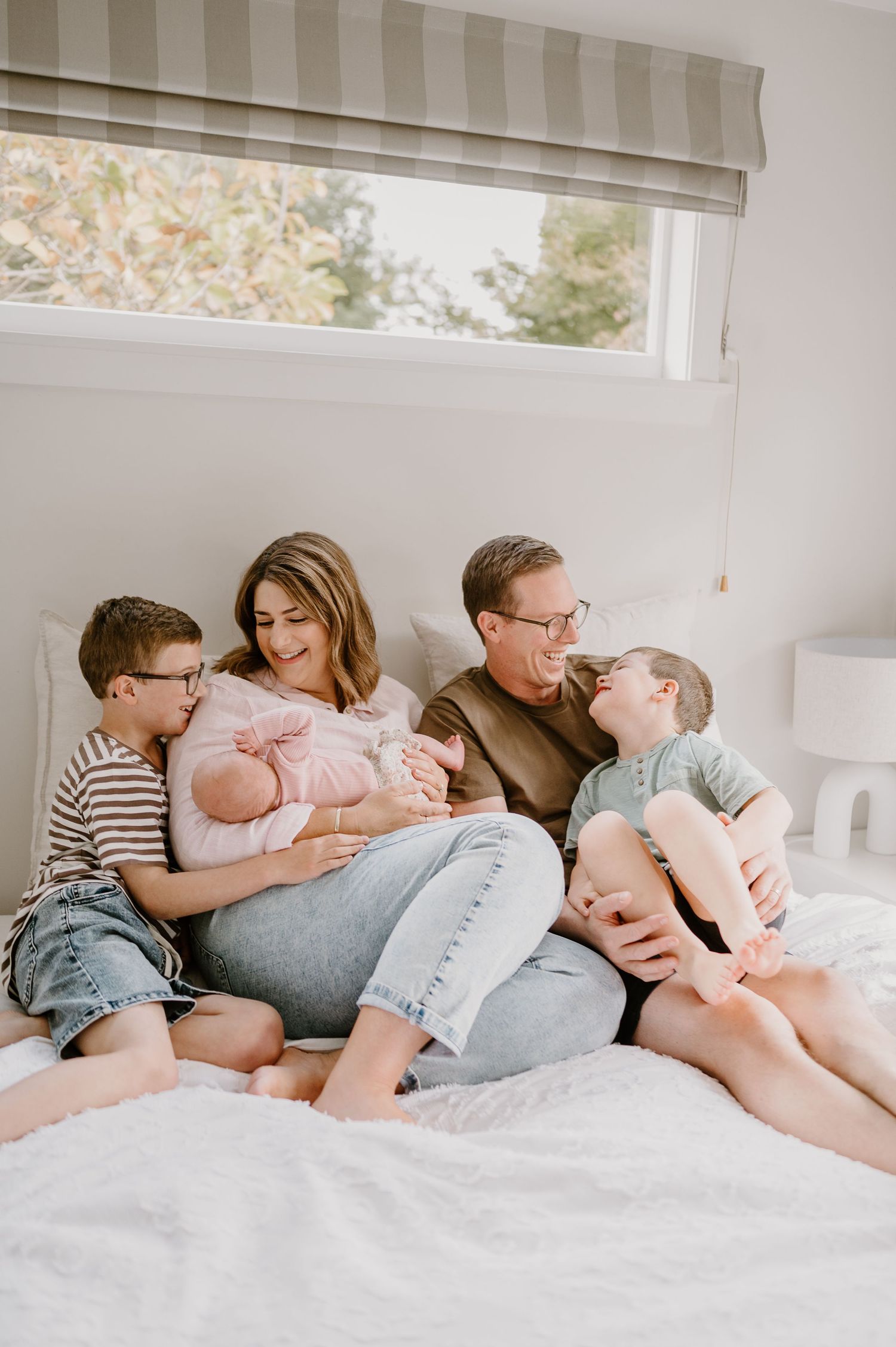 A family sharing a tender moment together on a bed beneath a window.